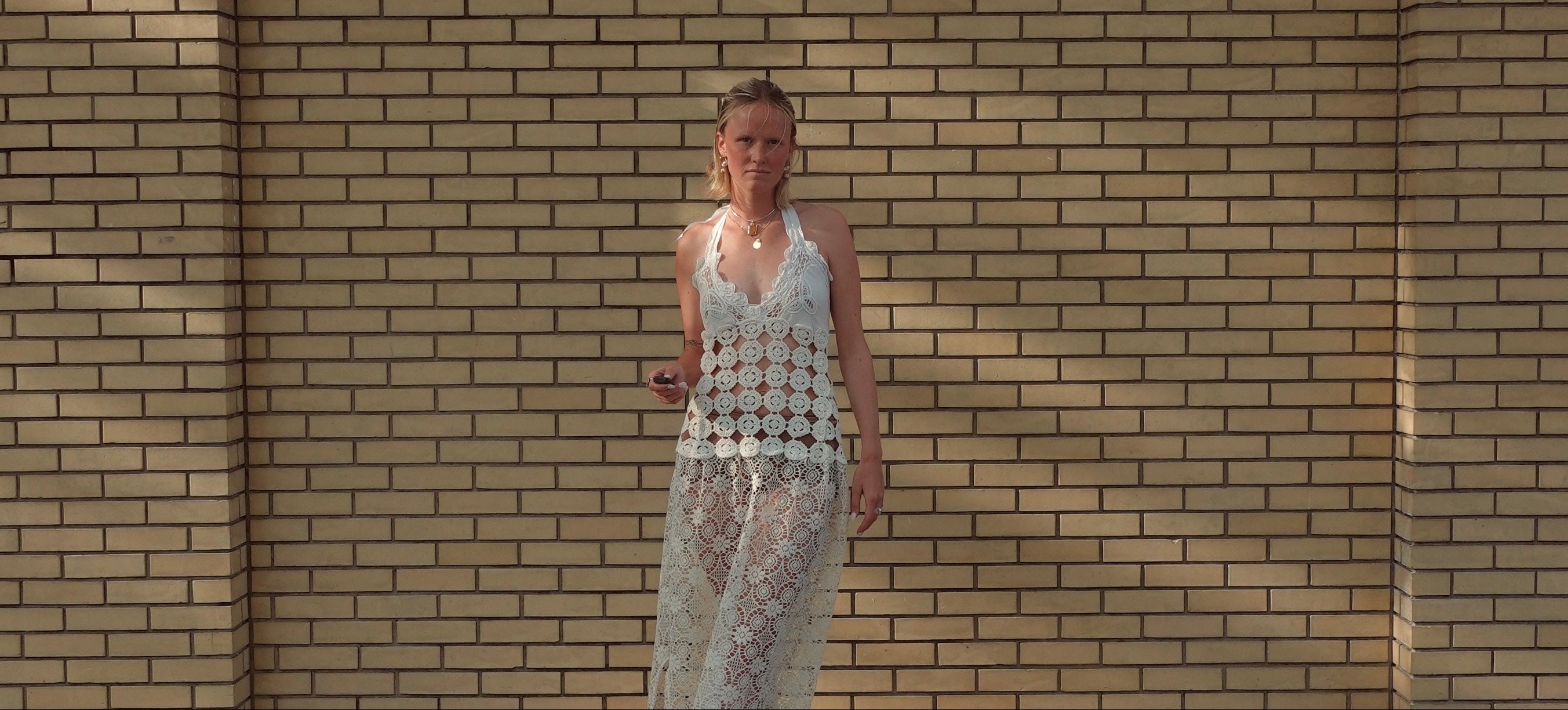 Woman in a patterned dress standing against a brick wall