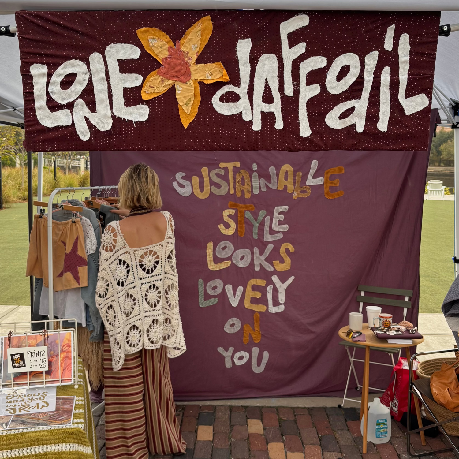 Person standing in front of a stall with 'Lone Daffodil' branding and text about sustainable style.